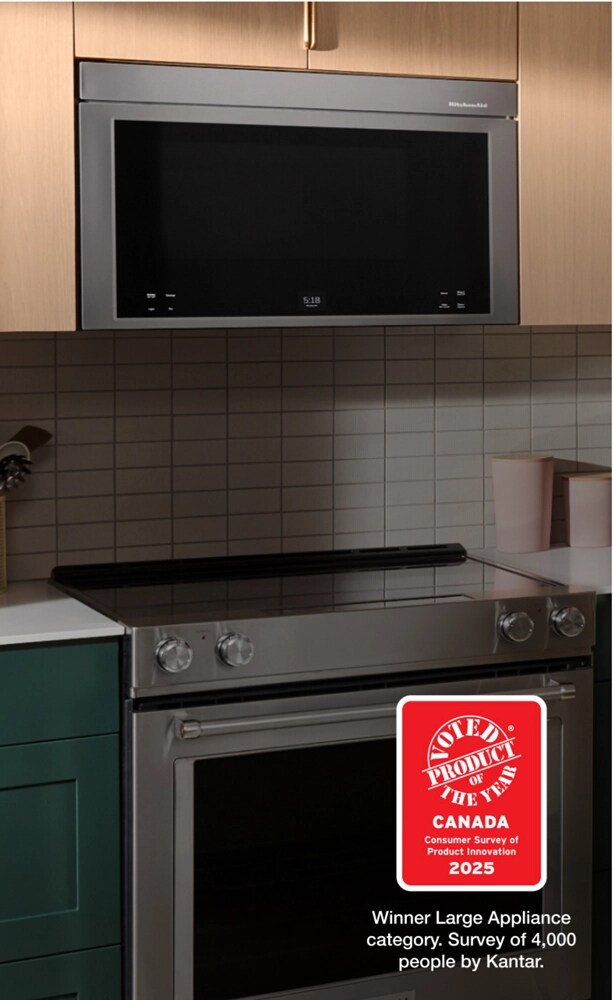 A kitchen with a KitchenAid Over-the-Range Microwave and KitchenAid Range. On the counters are plants, utensil holders, cutting boards and a dish cloth. There's an island with a plant, bowl of food, small dish with a sauce, a dish cloth, a cutting board with lemon and garlic among other various items.