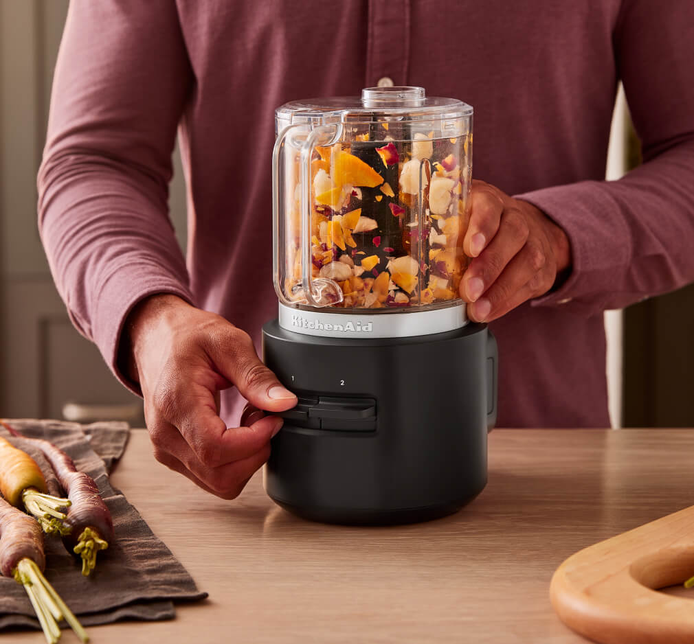 A person using a cordless food processor to chop up dried fruits and nuts. 