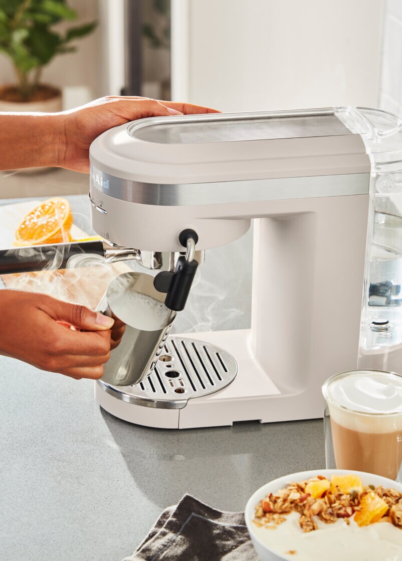 A person using a KiutchenAid® semi-automatic espresso machine to steam milk.
