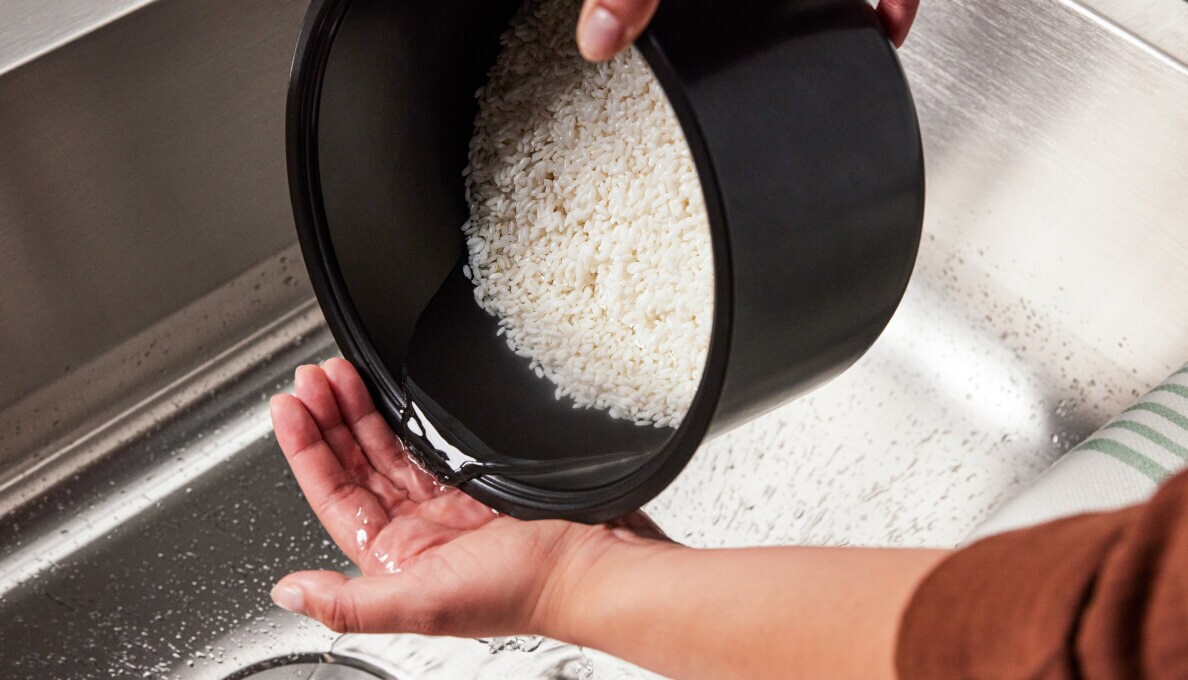A person rinsing rice in a small pot over the sink.