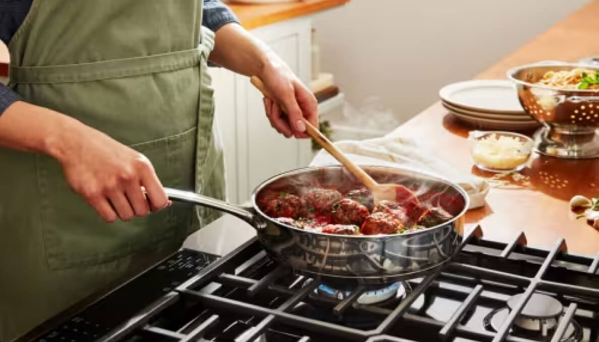 A person cooking a meal in a stainless steel pan over a gas burner.