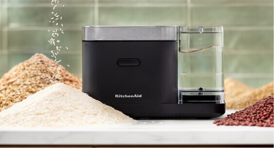 A closed grain and rice cooker with small mountains of rice and grains surrounding it.