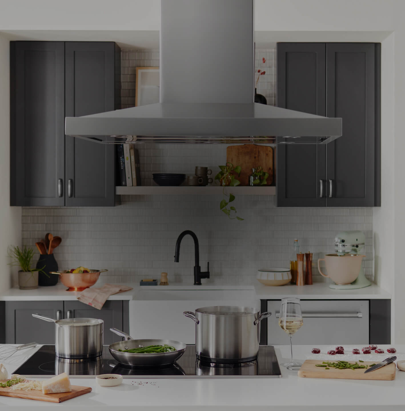 A ventilation hood above a cooktop with several tall saucepans on it.