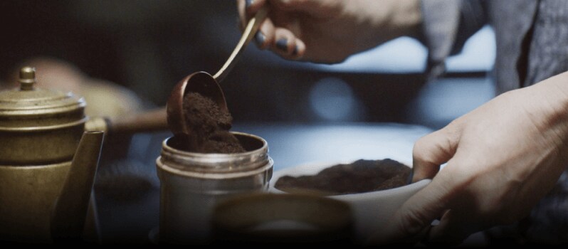 A person adding ground coffee into a bowl.