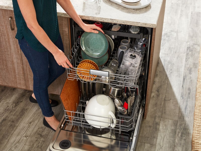Person loading rustic green plates into a dishwasher Person loading rustic green plates into a dishwasher