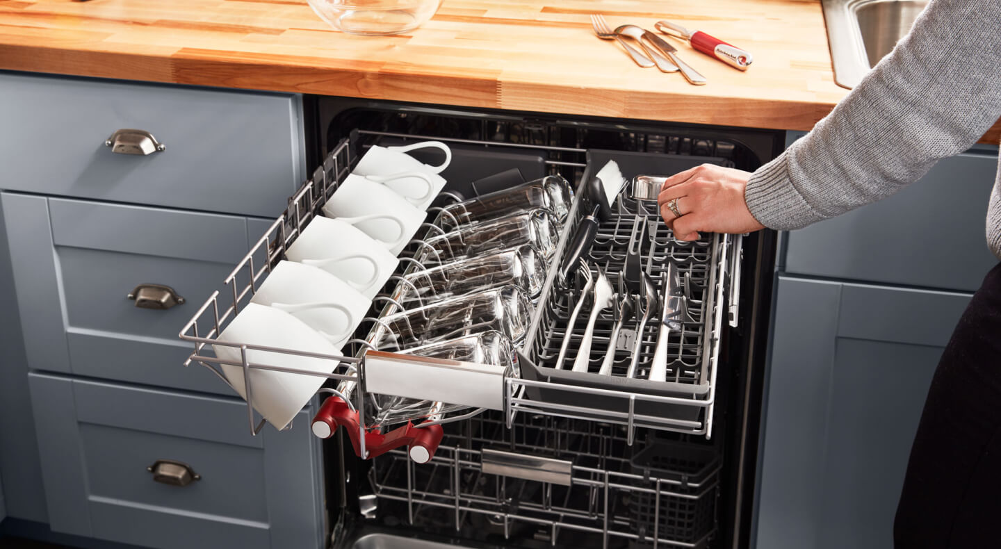 Person loading silverware into a dishwasher’s third rack Person loading silverware into a dishwasher’s third rack