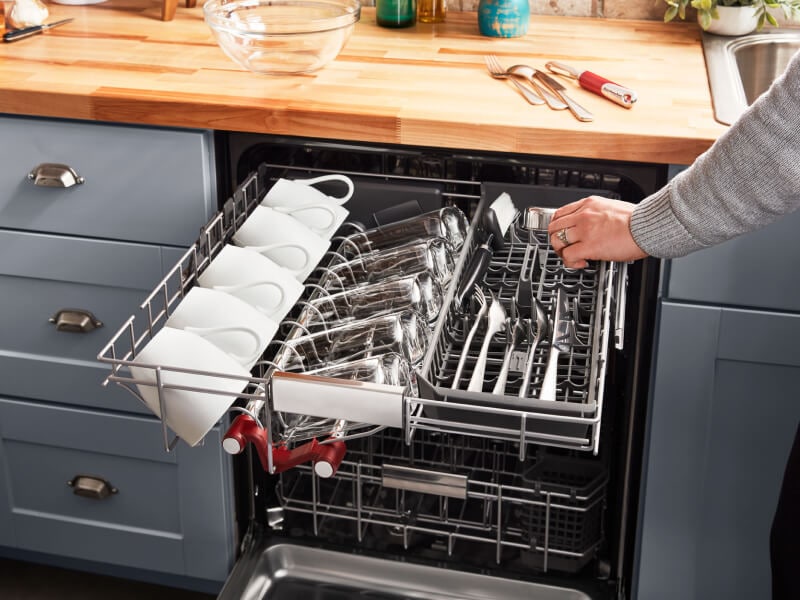 Person loading silverware into a dishwasher’s third rack Person loading silverware into a dishwasher’s third rack