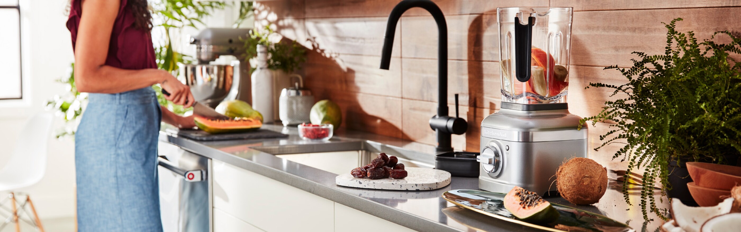 Woman cutting vegetables for prep, also a blender filled with unblended fruits and vegetables.
