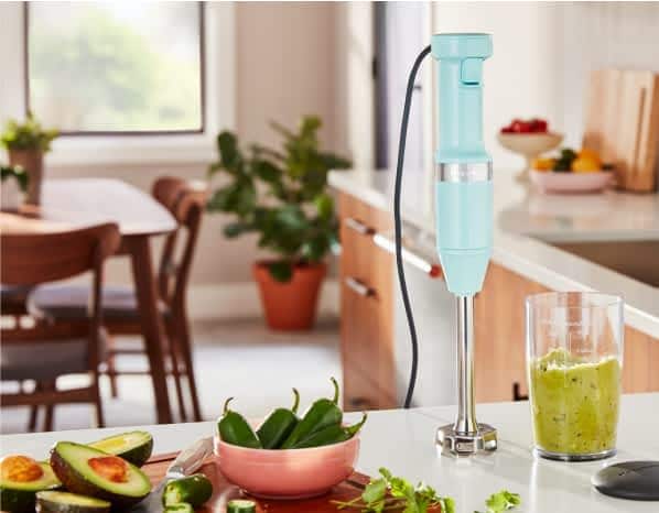 Avocados and jalapenos on a cutting board, with a KitchenAid® hand blender mixing guacamole.
