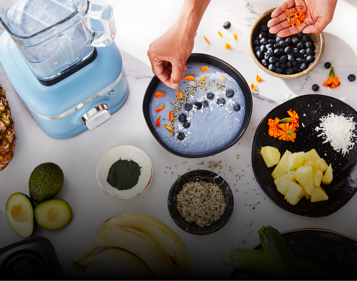 A person garnishing a blue smoothie bowl with fresh ingredients.