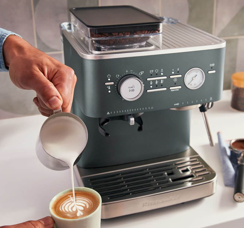 A person pouring milk into a mug to make latte art.