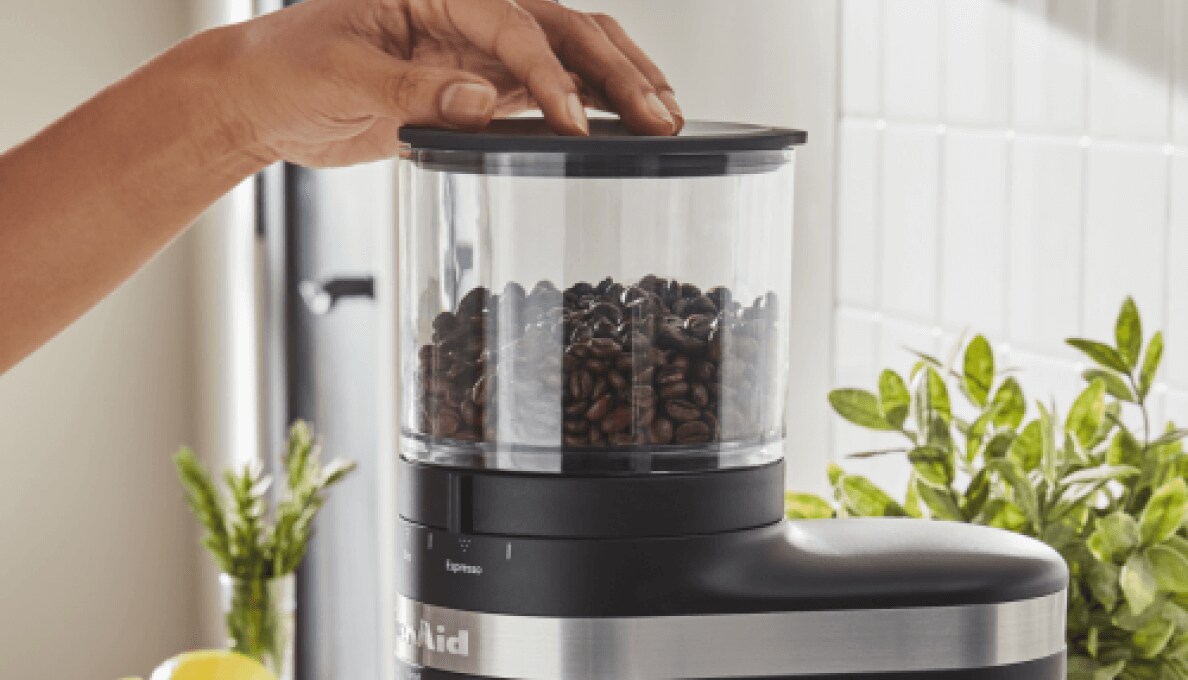 A woman preparing to process coffee beans in a black coffee grinder. 