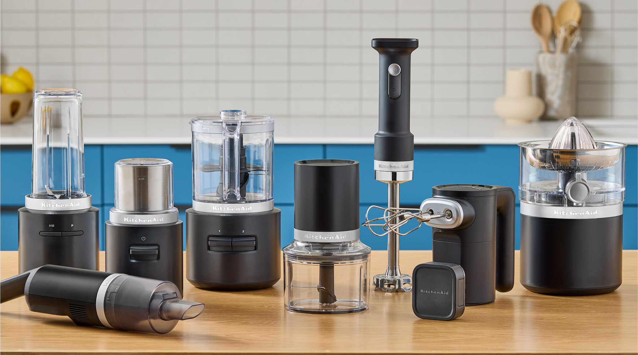The entire matte black KitchenAid Go™ Cordless lineup of appliances on a kitchen counter, with blue cabinets in the background.