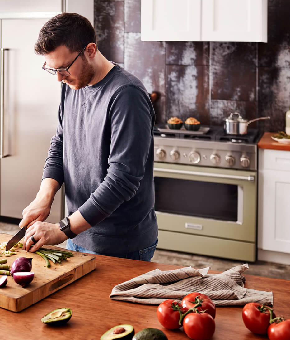 Man cutting vegetables with an avocado cream range in the background. 