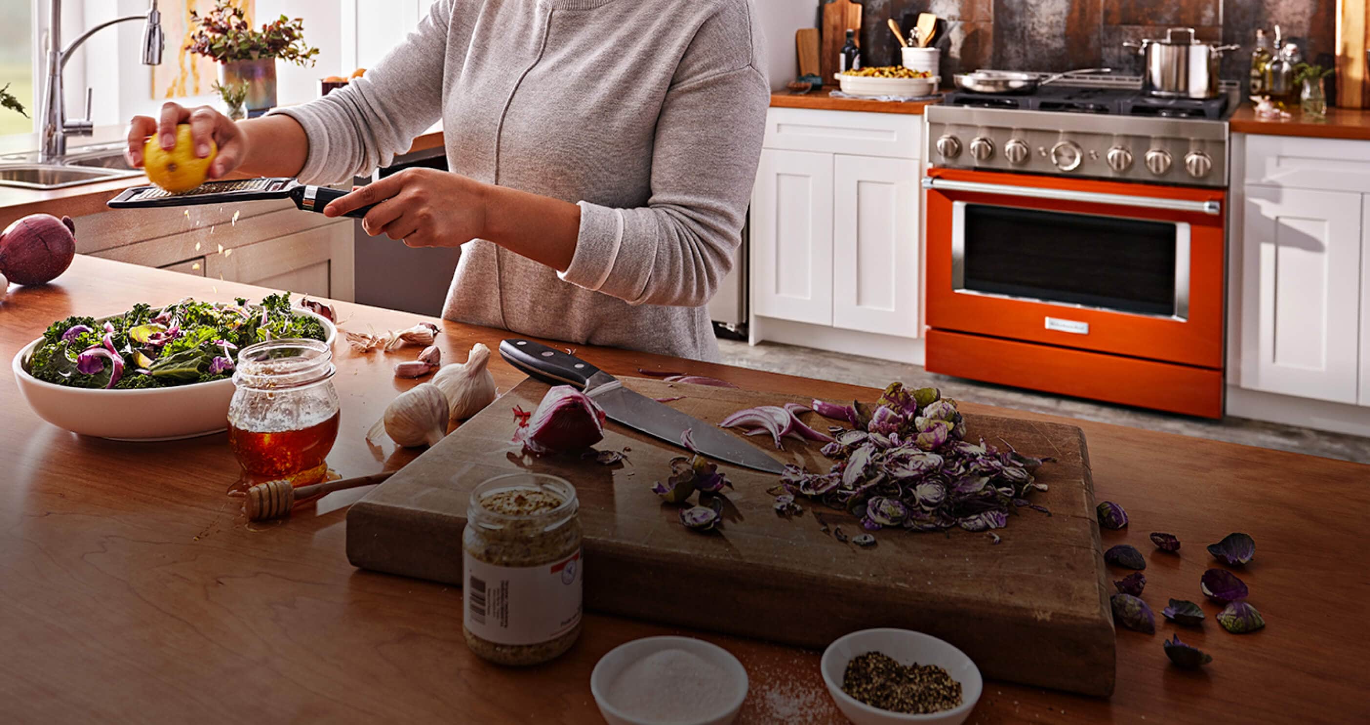 Woman zesting a lemon with scorched orange range in background.