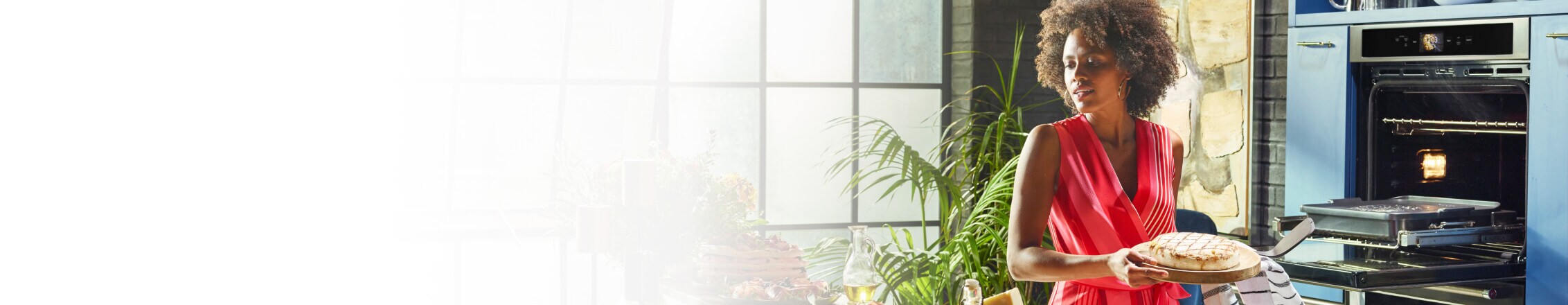 A young woman holding a wooden plate with freshly made bread from her KitchenAid® Smart Oven+.