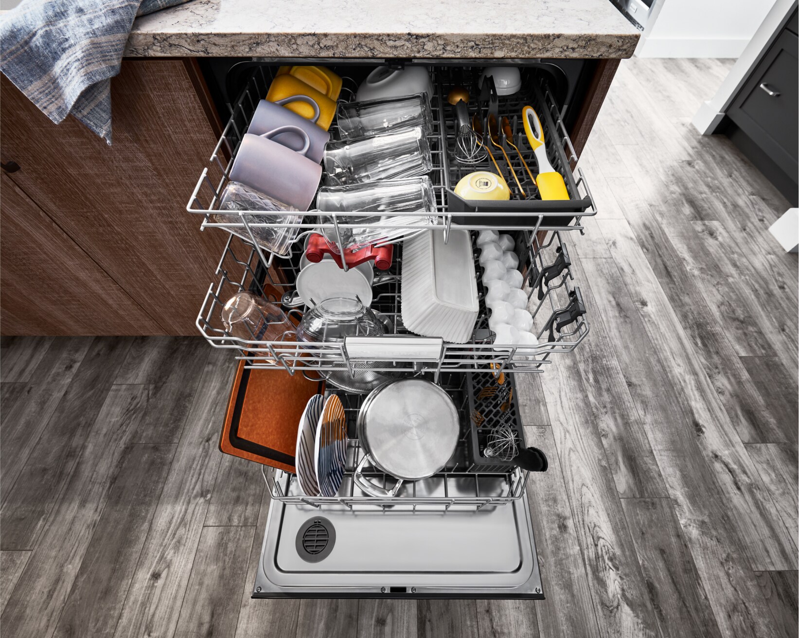 An open KitchenAid® dishwasher, with all racks full of dishware, glassware and utensils.