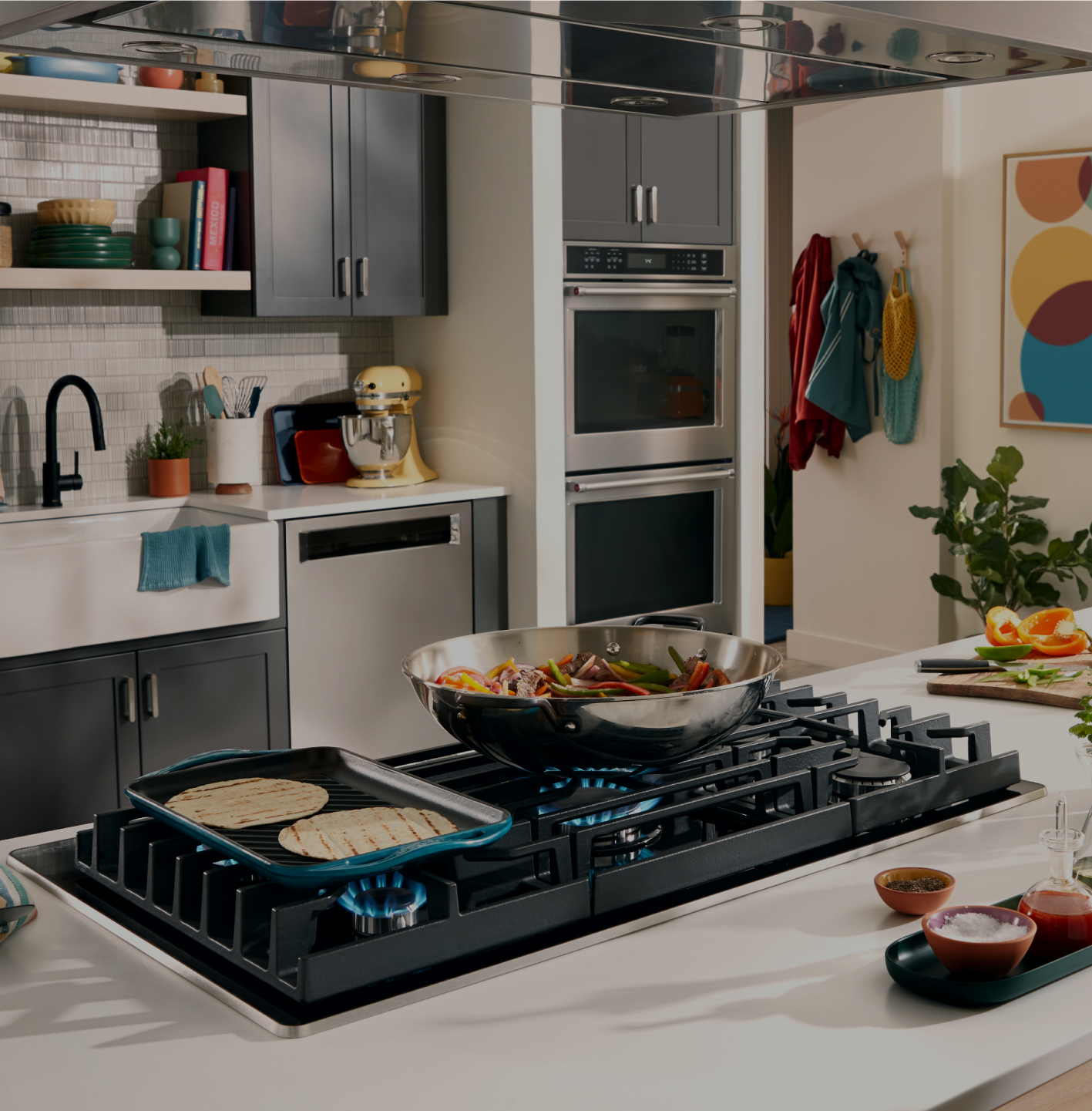 A griddle and saucepan on a KitchenAid gas cooktop.