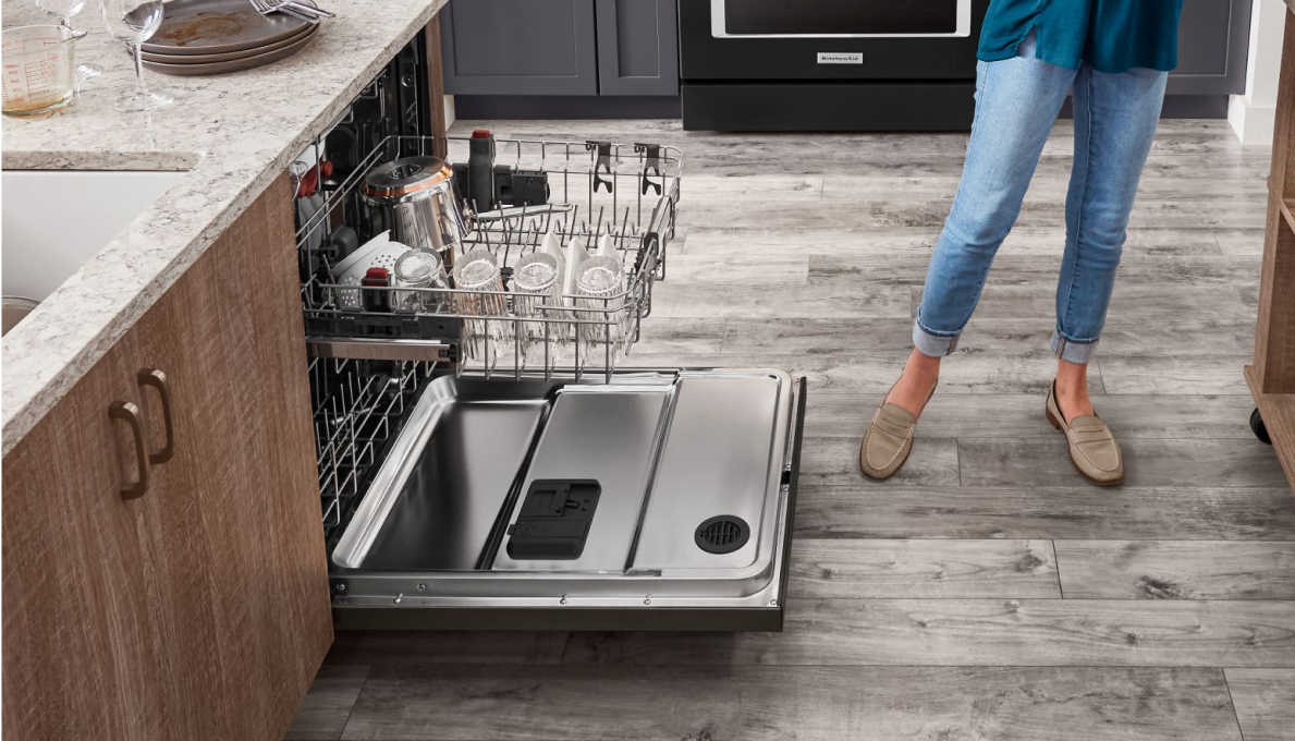 A person standing to the side of an open dishwasher.