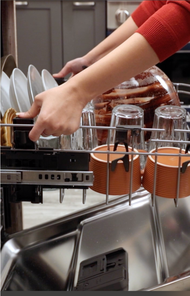 A person adjusting the middle rack of a dishwasher.