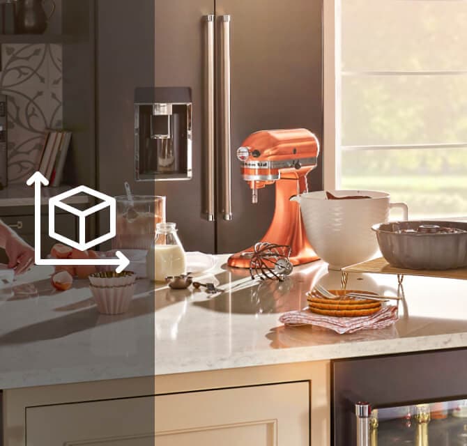 A person drizzling red icing on a cake and baking ingredients and a KitchenAid® stand mixer on the counter A person drizzling red icing on a cake and baking ingredients and a KitchenAid® stand mixer on the counter