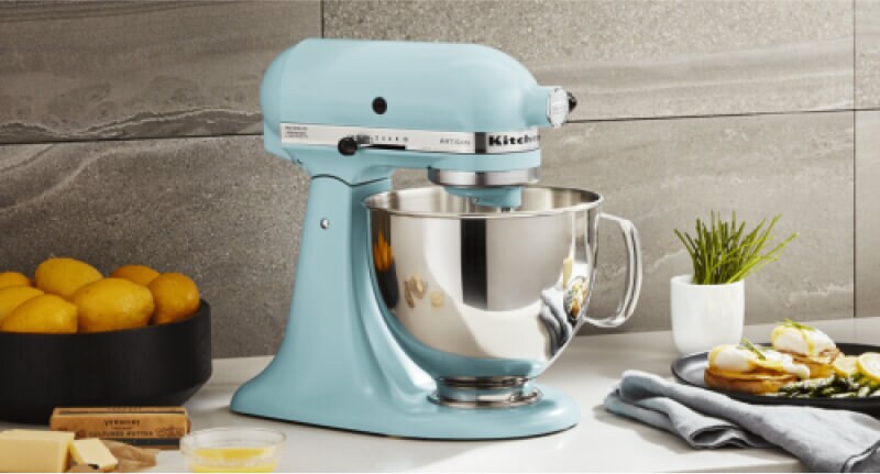 A blue KitchenAid® Stand Mixer on a countertop surrounded by different ingredients. 