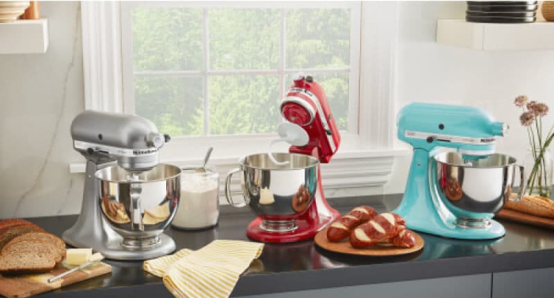 A trio of KitchenAid® Stand Mixers on a countertop with fresh baked bread on plates.