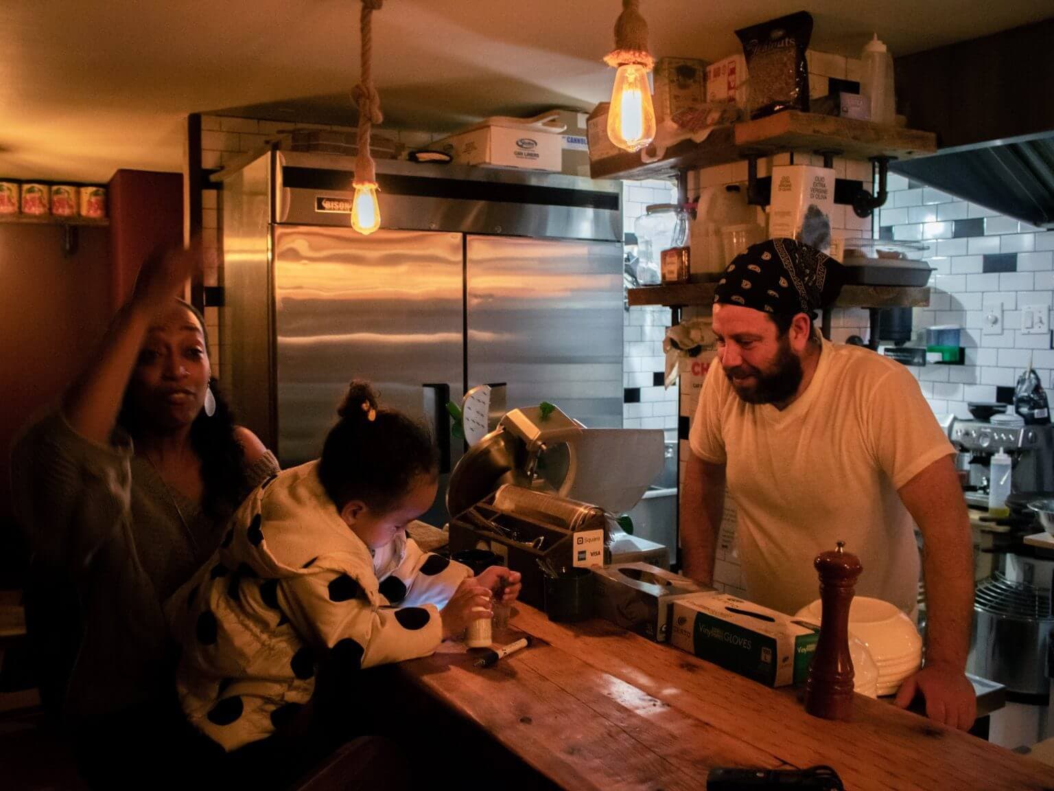 A man standing behind the register helping his two customers finish paying the tab.
