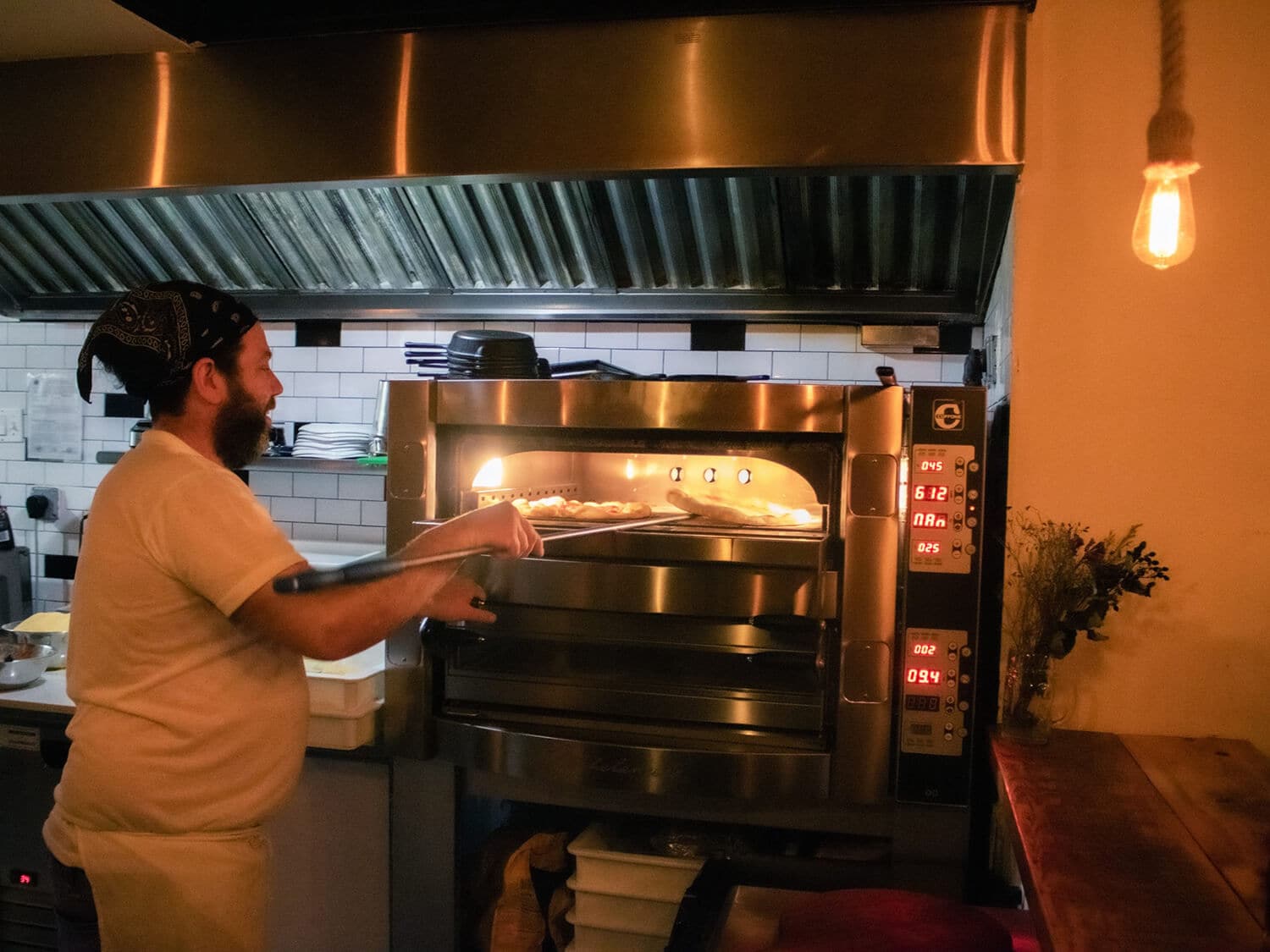 A man expertly working pizzas into a stainless steel pizza oven in a restaurant kitchen.