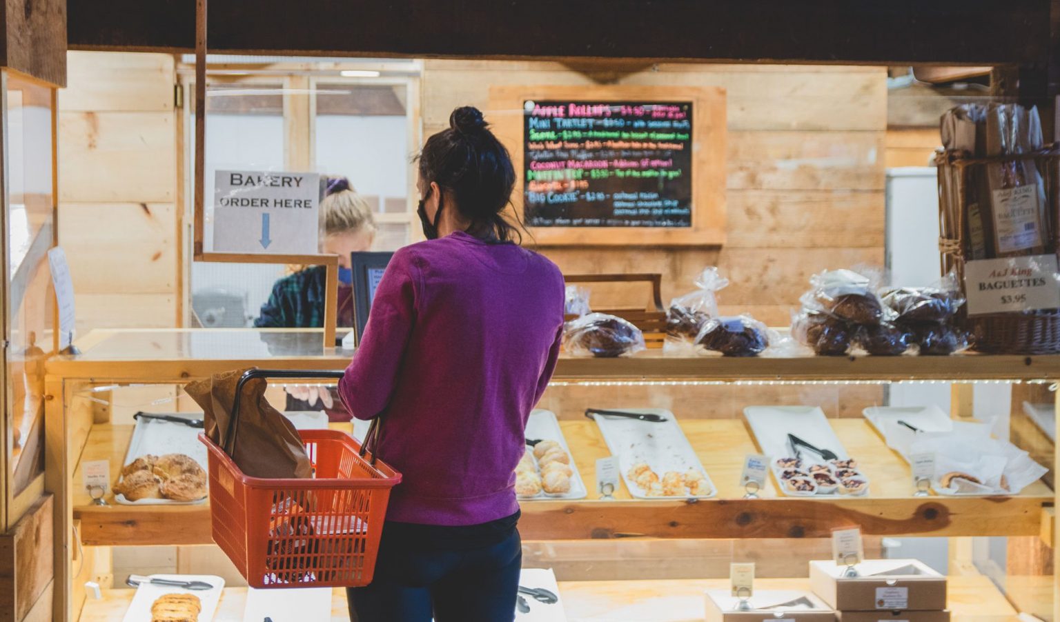 A young woman waiting for pastries as she carries her shopping basket.