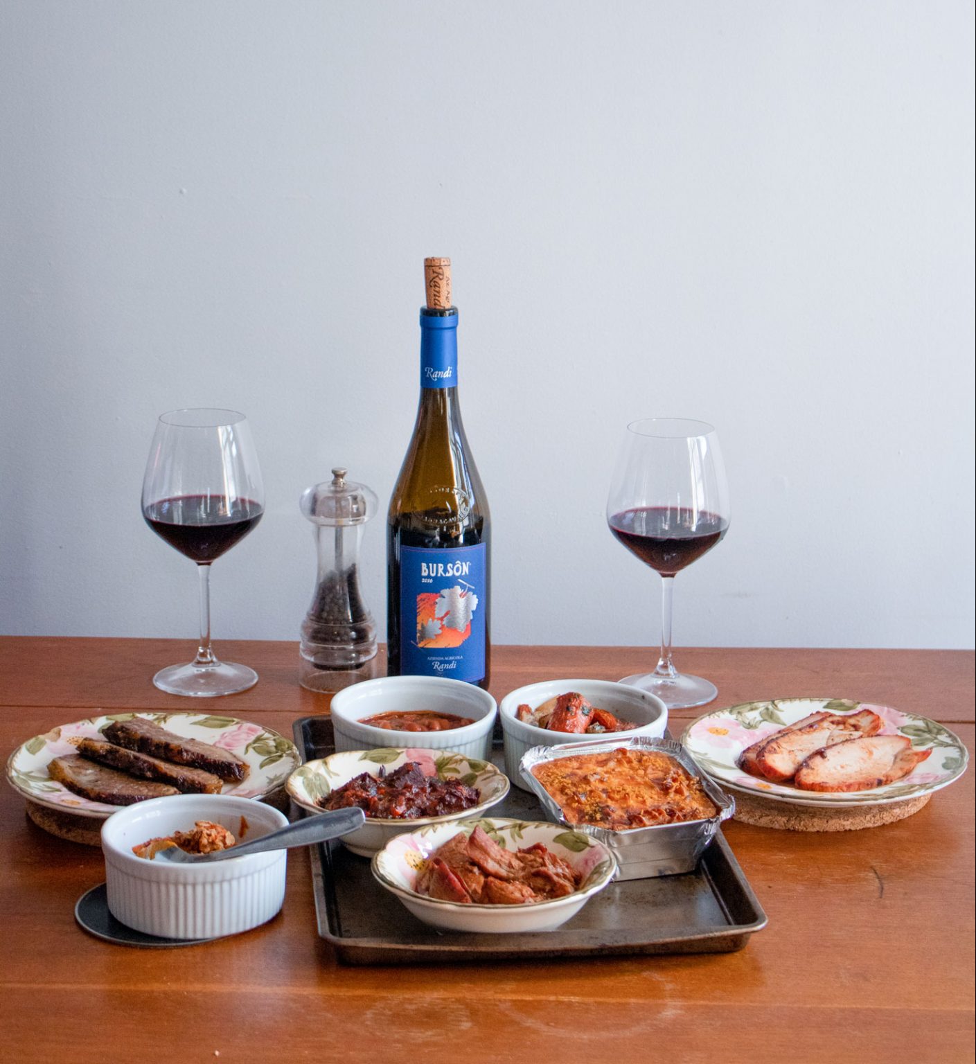 A table with an open bottle, two filled wine glasses and other dishes.