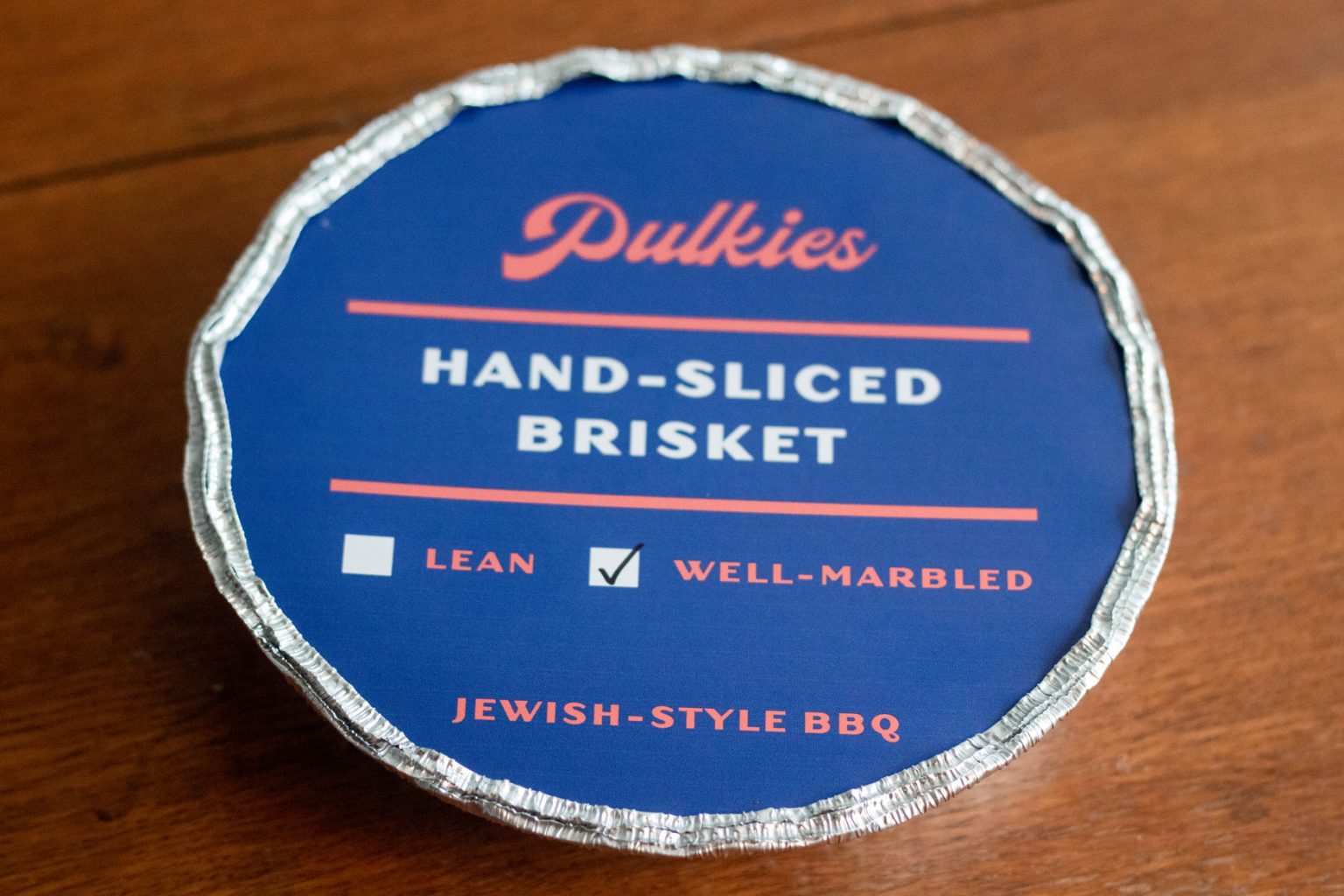 A sealed circular foil container filled with hand-sliced brisket.