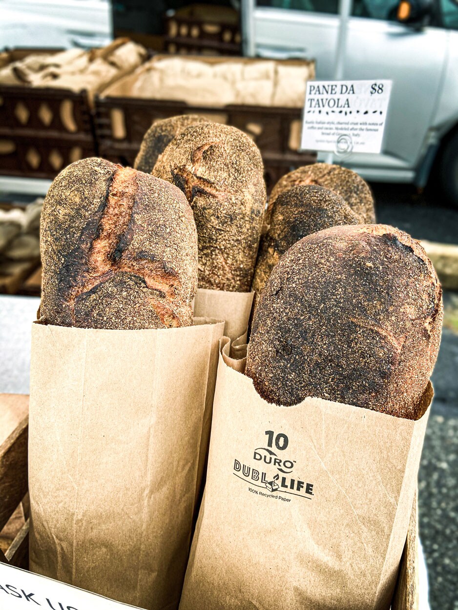 Four loaves of baked bread resting in individual brown paper bags.