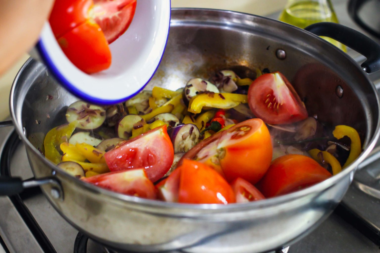 A large pot cooking sliced tomatoes, eggplant and more ingredients.