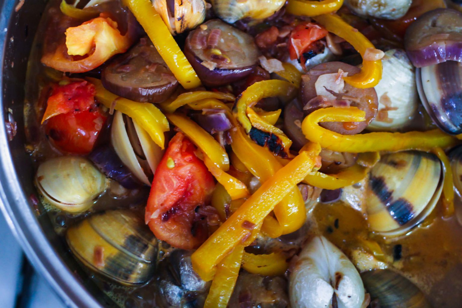 Clams, sliced peppers, eggplant and other ingredients boiling in a pot.