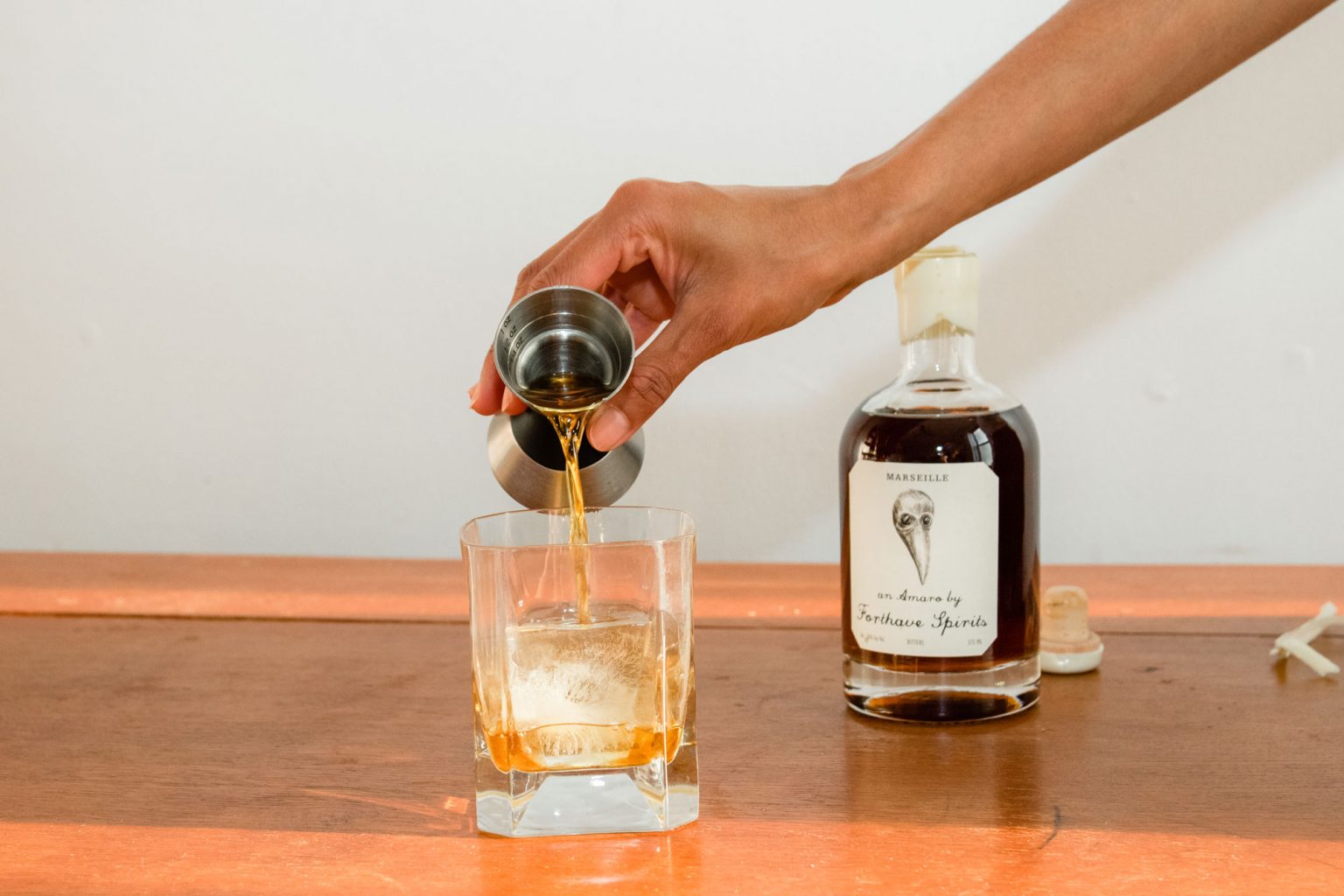 A person pouring Forthave Spirit liquor into a whiskey glass.