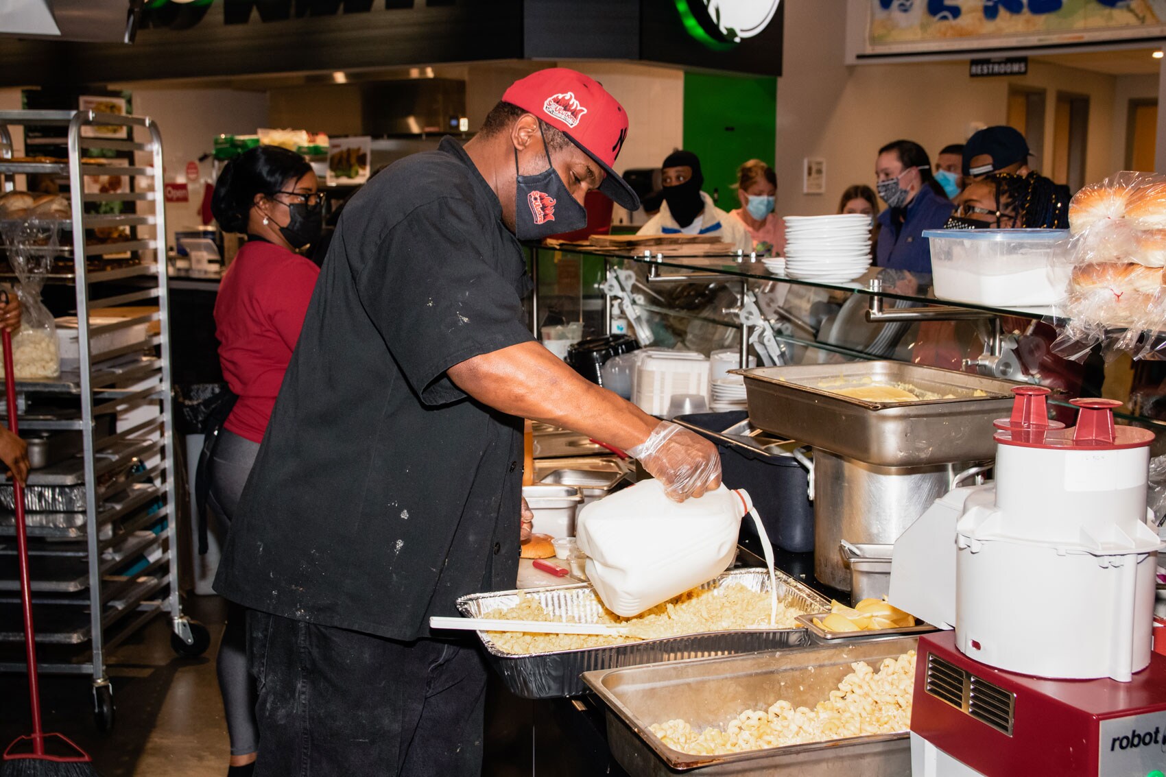 Sley adding milk to a large tray of mac and cheese.