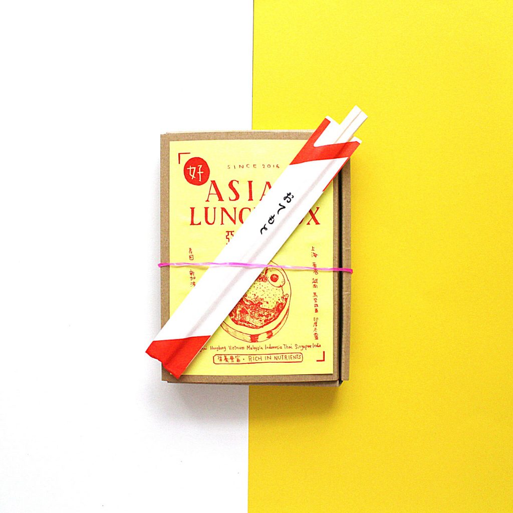 A cardboard lunchbox with chopsticks resting on top.