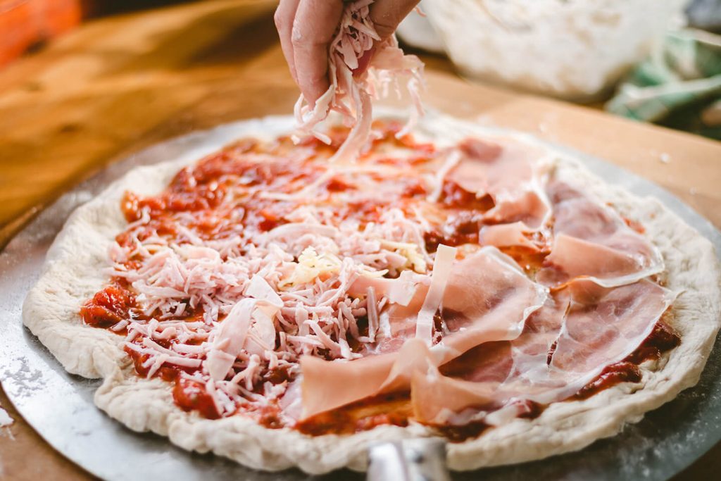 A person making a pizza from scratch, dressing it with sauce and other fixings.