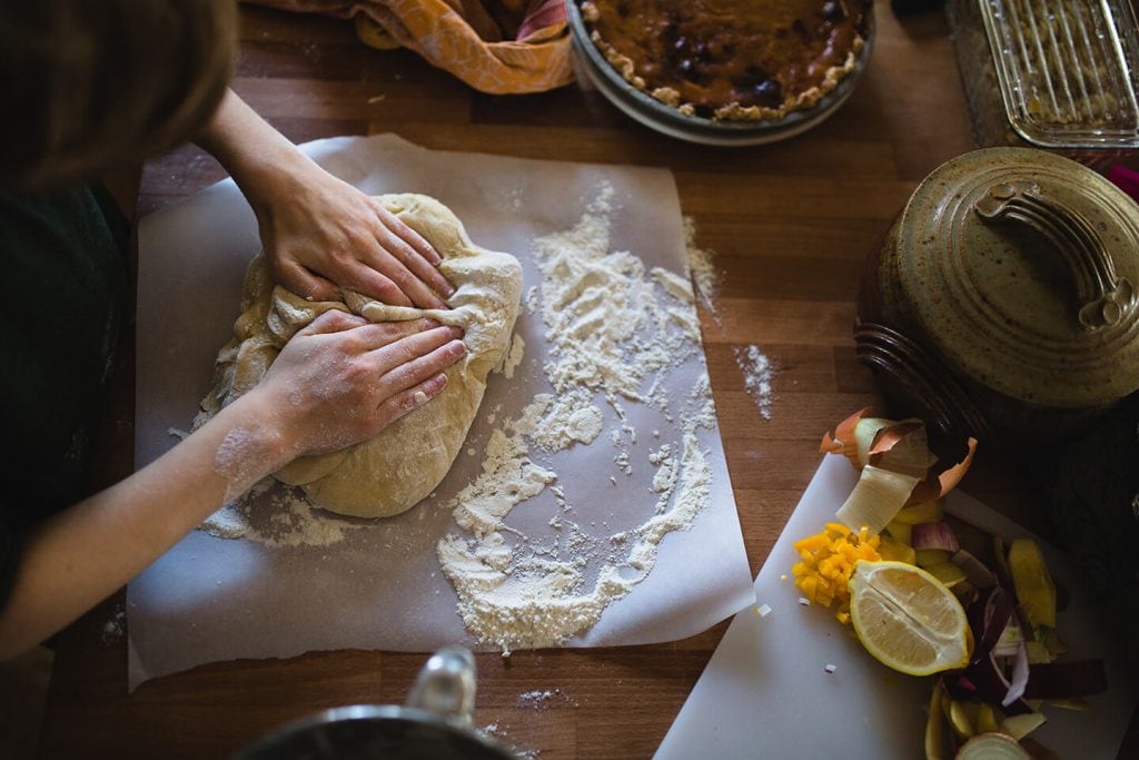 A person gently working dough with flour on parchment paper.