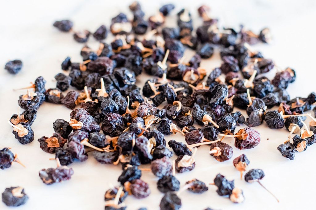 Dried black goji berries scattered across a white table.