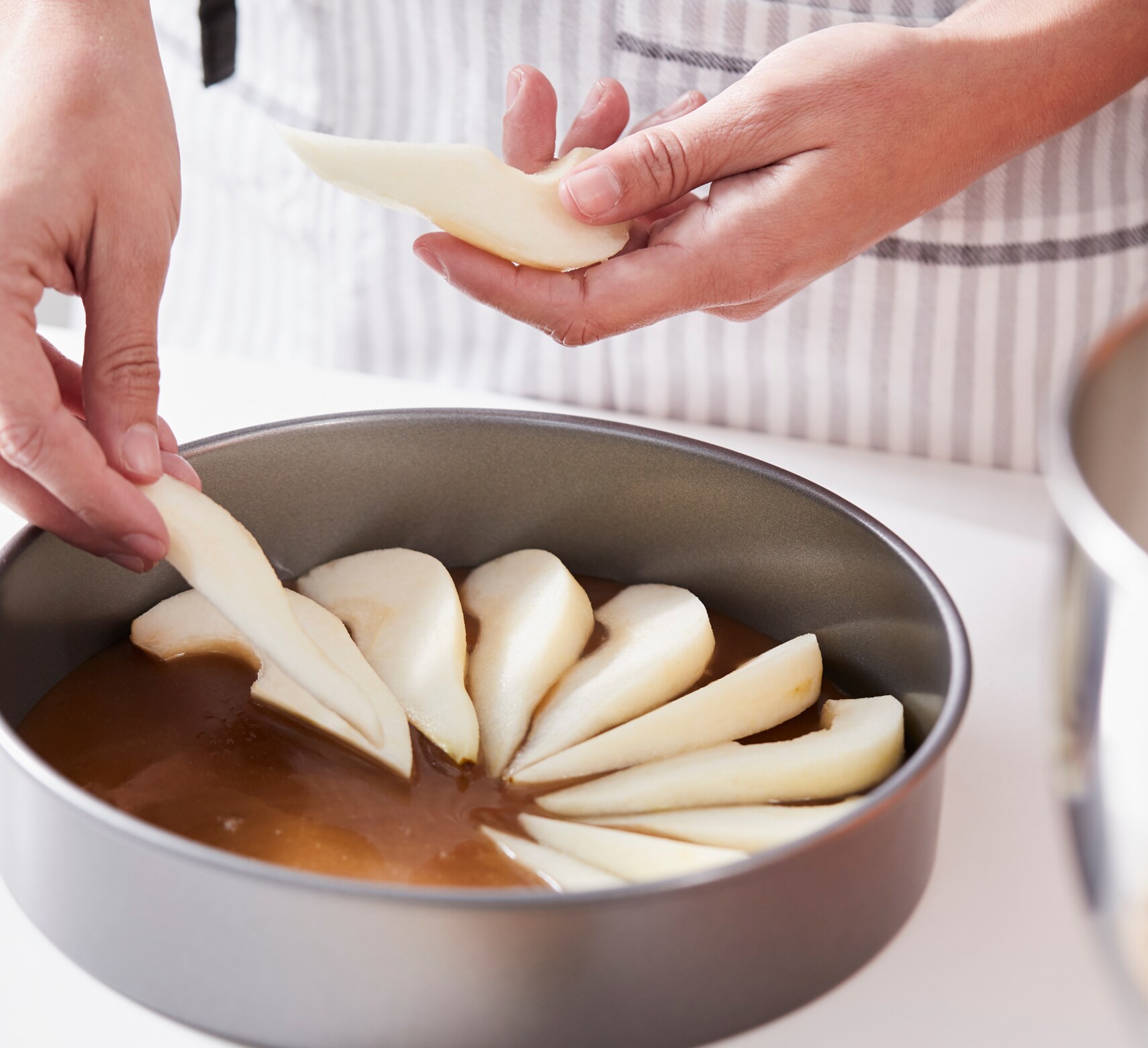 Person laying sliced pears in a cake tin
