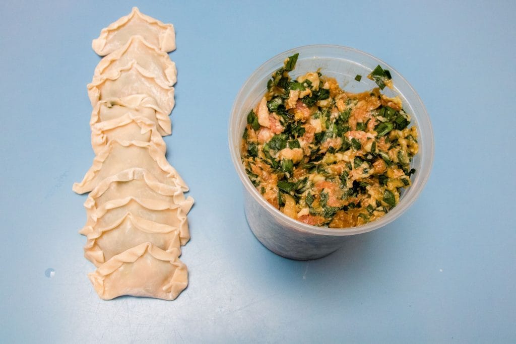 Freshly wrapped dumplings resting on the table next to a container of filling.
