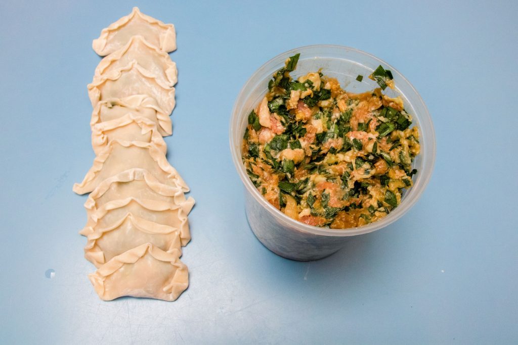 Freshly wrapped dumplings resting on the table next to a container of filling.