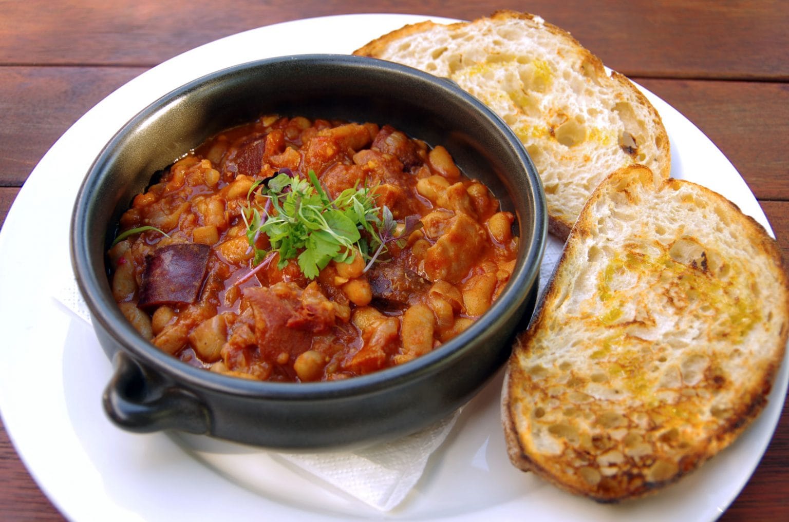 A black bowl filled with spicy New Orleans red beans and rice with a side of toasted bread.