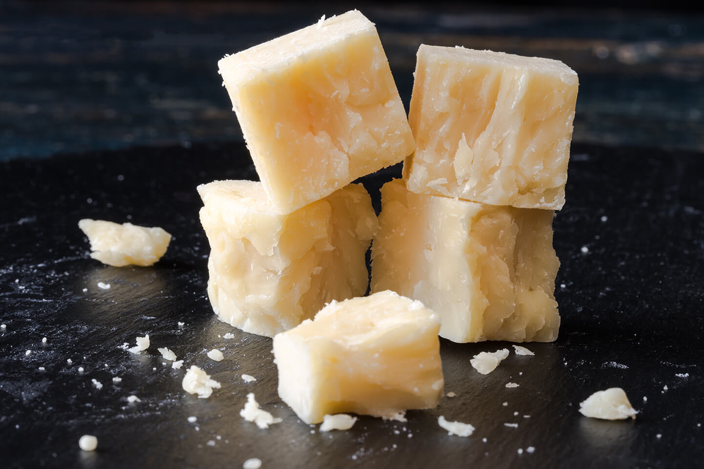 Crumbling cheese cut up into delicate cubes on a dark wooden cutting board.