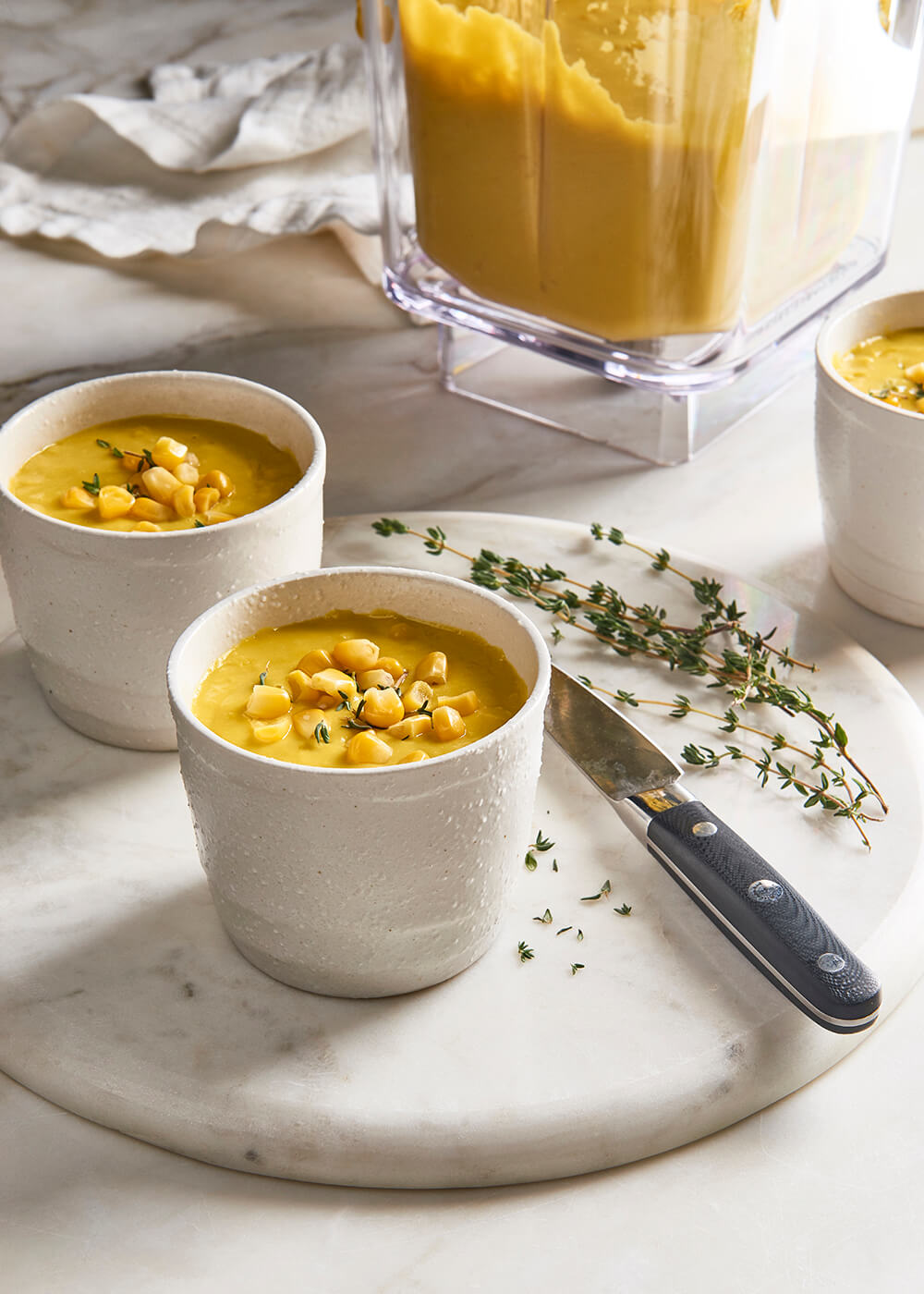 Two bowls of soup garnished with corn and thyme.