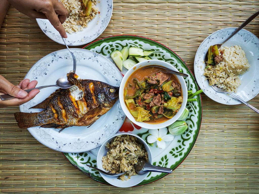 A roasted whole fish resting on a white plate accompanied by curry, rice and vegetables.