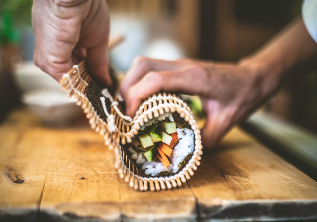 Fresh sushi being wrapped together using a bamboo rolling mat.