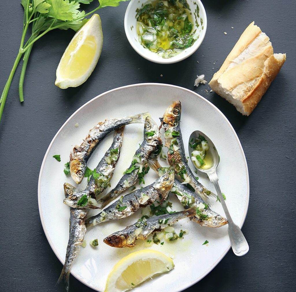 Roasted sardines on a clean white plate garnished with sliced lemons and cilantro.